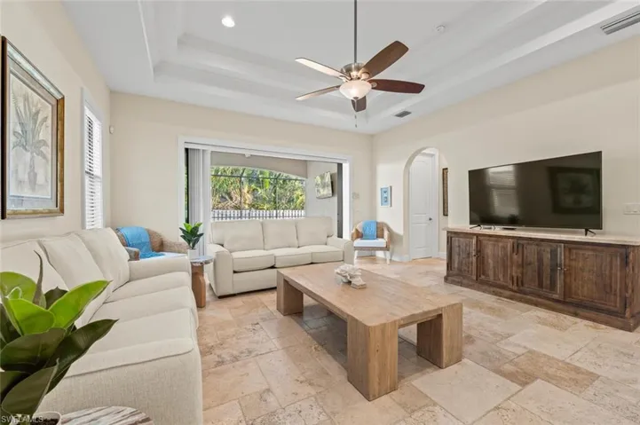 Living room with a tray ceiling, stone tile flooring, arched walkways, ceiling fan, and recessed lighting