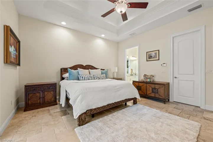 Bedroom with stone tile floors, a raised ceiling, recessed lighting, ornamental molding, and ensuite bath