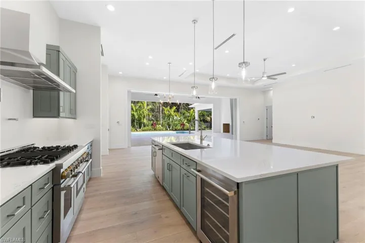 Kitchen with a center island with sink, hanging light fixtures, sink, appliances with stainless steel finishes, and wine cooler. Gas range hood is not completed yet as well as pot filler faucet.