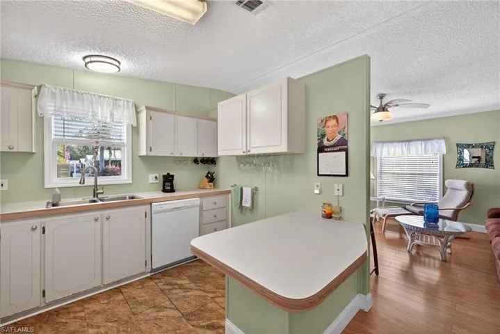 Kitchen with light countertops, a textured ceiling, white cabinets, dishwasher, and ceiling fan