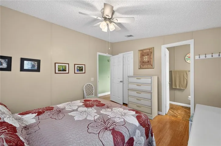 Bedroom with a textured ceiling, ceiling fan, wood finished floors, and connected bathroom