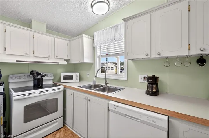 Kitchen featuring white appliances, light countertops, a textured ceiling, and white cabinets