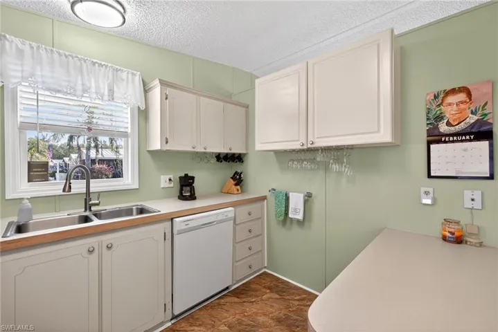 Kitchen featuring a textured ceiling, light countertops, dishwasher, and white cabinets