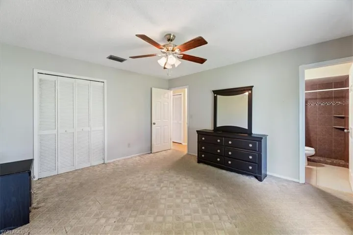 Unfurnished bedroom with light colored carpet, a ceiling fan, a textured ceiling, a closet, and connected bathroom