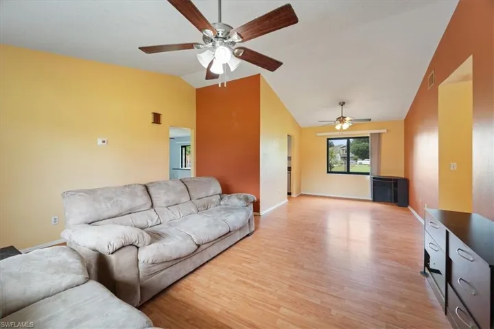 Living room with lofted ceiling, light wood finished floors, and a ceiling fan