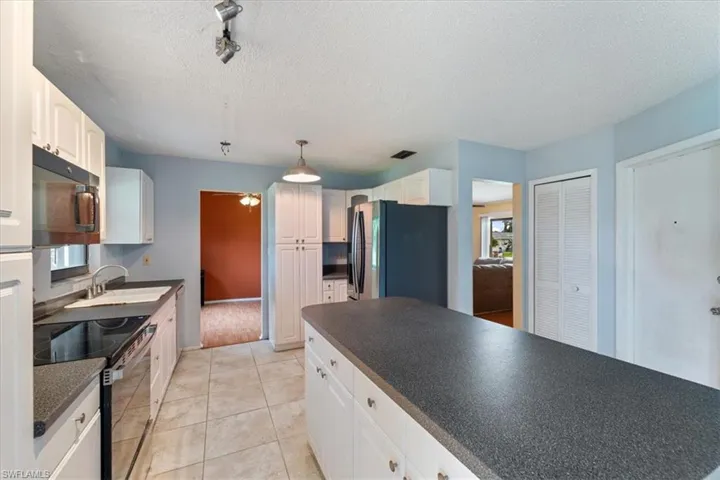 Kitchen with range with electric cooktop, freestanding refrigerator, dark countertops, a textured ceiling, and white cabinets