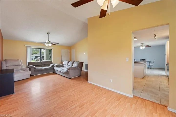 Living area with vaulted ceiling, a ceiling fan, and light wood-style floors