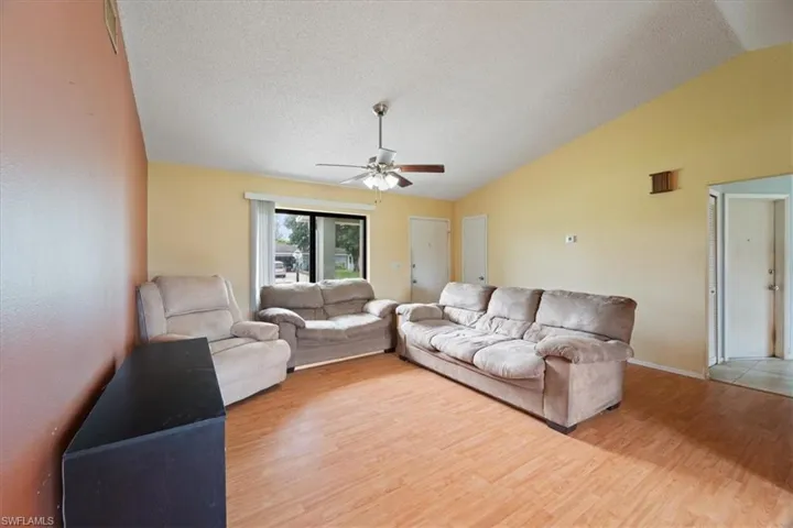 Living room with vaulted ceiling, wood finished floors, a textured ceiling, and ceiling fan