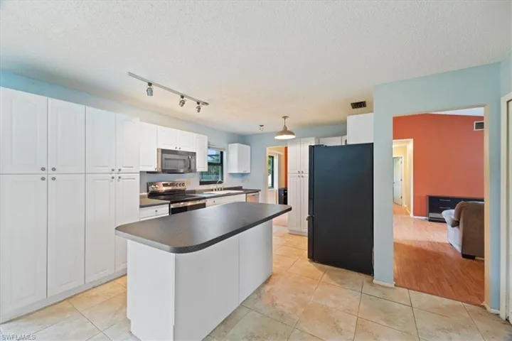 Kitchen with white cabinetry, stainless steel appliances, dark countertops, track lighting, and a kitchen island