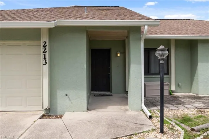 Property entrance with roof with shingles, stucco siding, a garage, and a porch