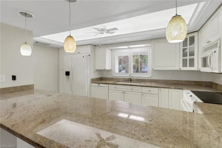 Kitchen featuring stone counters, white appliances, a sink, a raised ceiling, and glass insert cabinets
