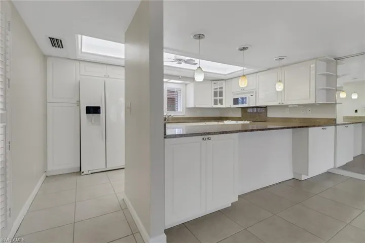 Kitchen featuring light tile patterned floors, visible vents, glass insert cabinets, white cabinetry, and white appliances