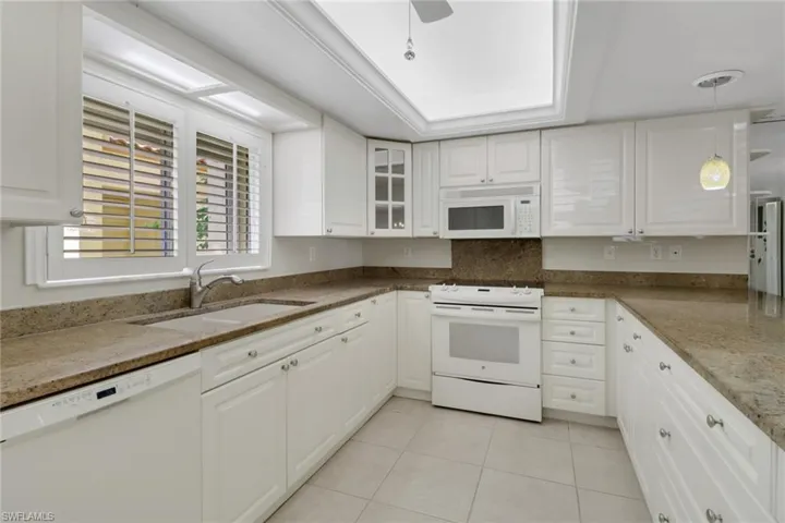 Kitchen featuring white appliances, light tile patterned floors, white cabinets, and a sink