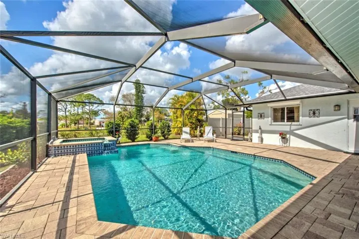 View of pool with an in ground hot tub, glass enclosure, and a patio area