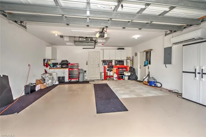 Garage with a garage door opener, electric panel, and an AC wall unit