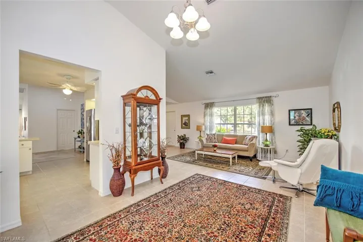 Living room featuring light tile patterned floors, ceiling fan with notable chandelier, and high vaulted ceiling