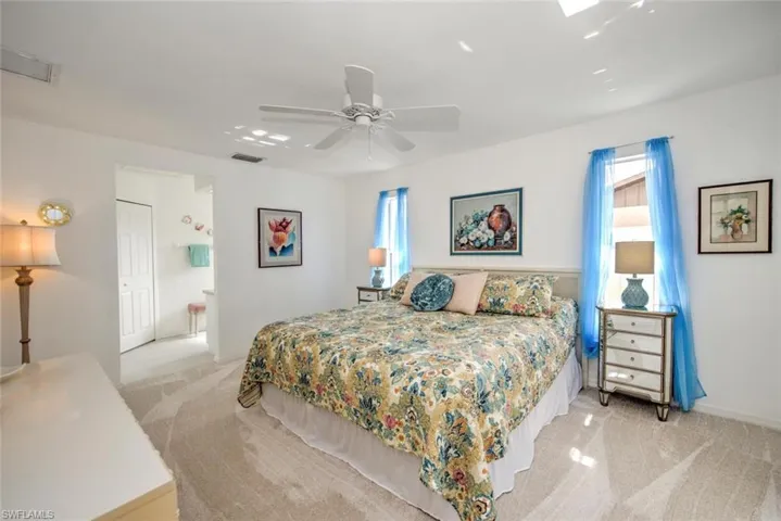 Carpeted bedroom featuring multiple windows, connected bathroom, and ceiling fan