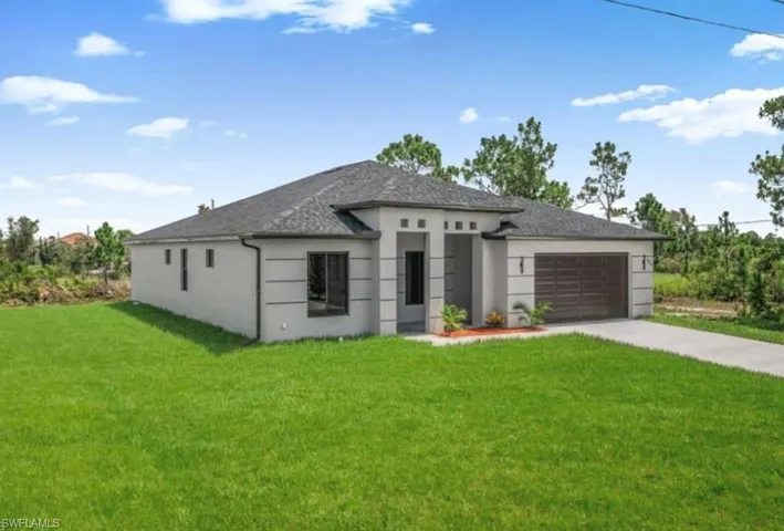 Prairie-style home with a front lawn, driveway, a garage, stucco siding, and roof with shingles