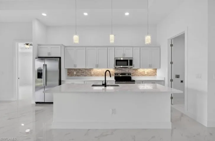 Kitchen featuring light marble finish flooring, stainless steel appliances, decorative backsplash, light stone counters, and hanging light fixtures