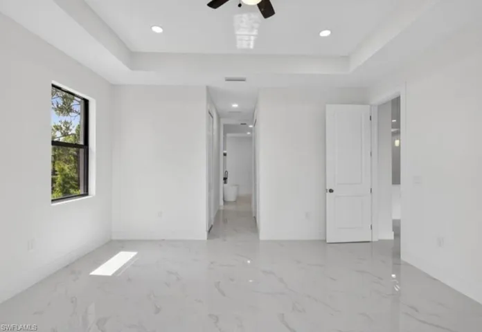Unfurnished bedroom with light marble finish floors, a tray ceiling, recessed lighting, ceiling fan, and ensuite bath