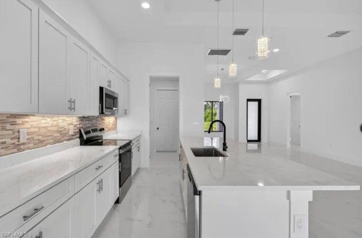 Kitchen with stainless steel appliances, light marble finish floors, a large island, a raised ceiling, and recessed lighting