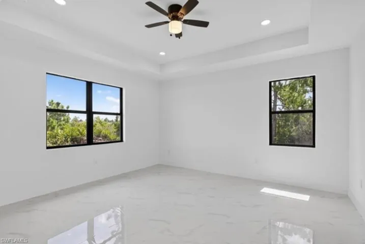 Spare room with a raised ceiling, light marble finish floors, recessed lighting, and a ceiling fan
