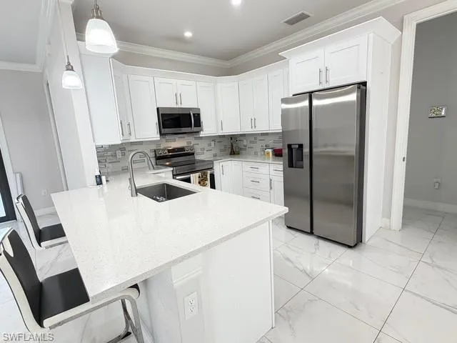 Kitchen featuring appliances with stainless steel finishes, white cabinets, tasteful backsplash, light stone counters, and crown molding