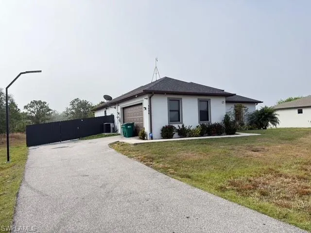 Ranch-style home featuring an attached garage, a front yard, asphalt driveway, a gate, and stucco siding