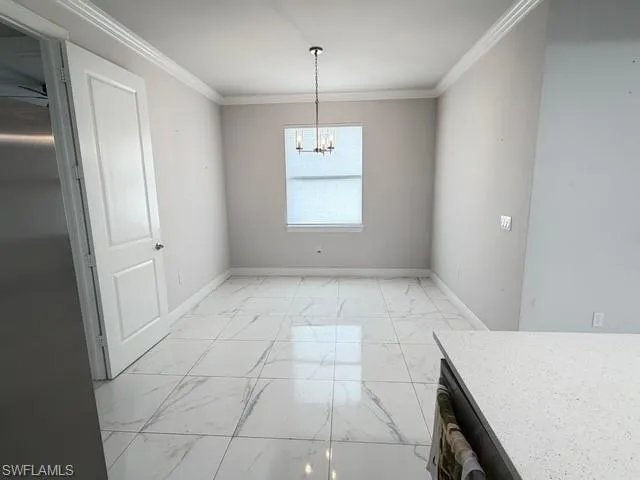 Unfurnished dining area with light marble finish floors, crown molding, and a chandelier