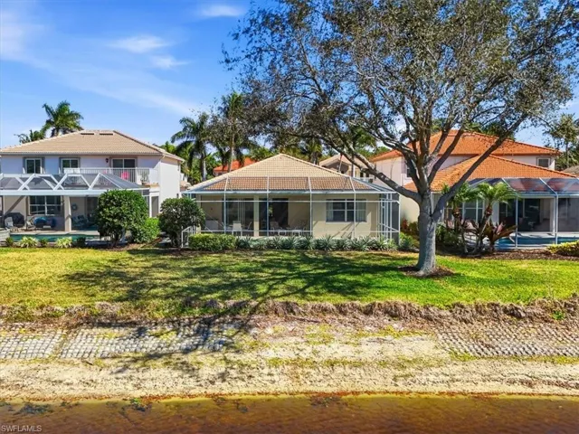 Back of property featuring a sunroom, a water view, glass enclosure, and a lawn