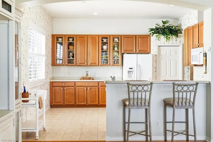 Kitchen featuring wood finish cabinets, a kitchen breakfast bar, white appliances, tasteful backsplash, and a peninsula