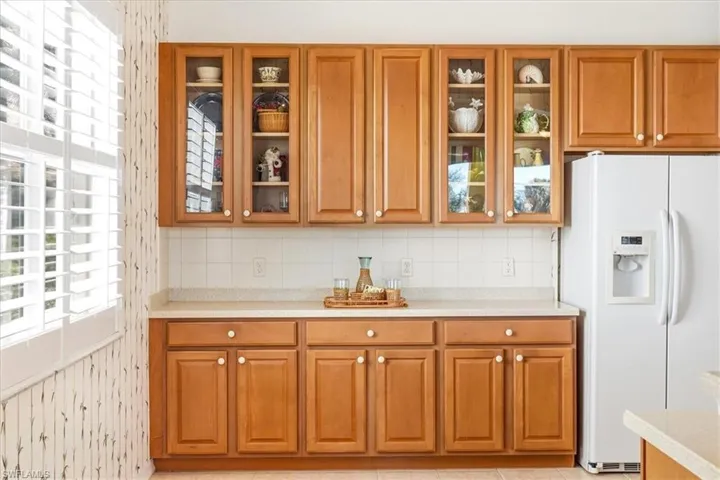 Kitchen featuring white fridge with ice dispenser, decorative backsplash, wood finish cabinetry, glass fronted cabinets, and plenty of natural light