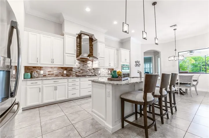 Kitchen featuring appliances with stainless steel finishes, wall chimney exhaust hood, backsplash, white cabinetry, and ornamental molding
