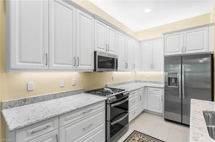 Kitchen featuring appliances with stainless steel finishes, white cabinetry, light stone countertops, light tile patterned floors, and recessed lighting