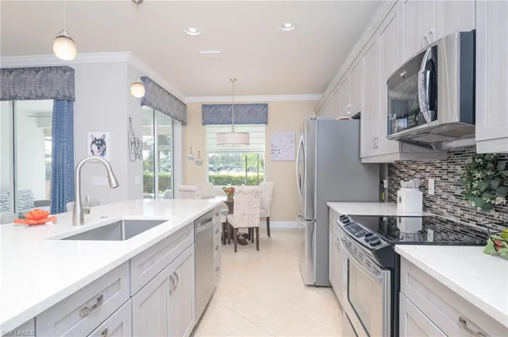 Kitchen with appliances with stainless steel finishes, hanging light fixtures, ornamental molding, and sink
