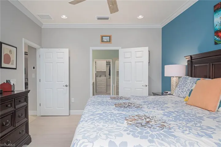 Bedroom with connected bathroom, light hardwood / wood-style floors, ceiling fan, and ornamental molding