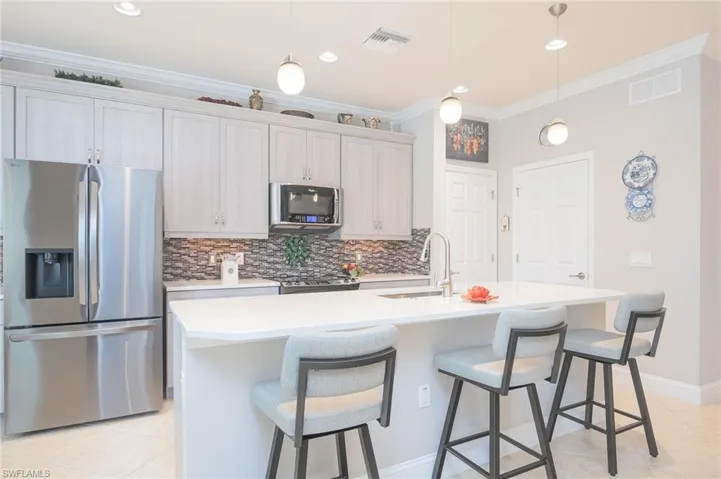 Kitchen featuring ornamental molding, stainless steel appliances, a kitchen island with sink, sink, and decorative light fixtures
