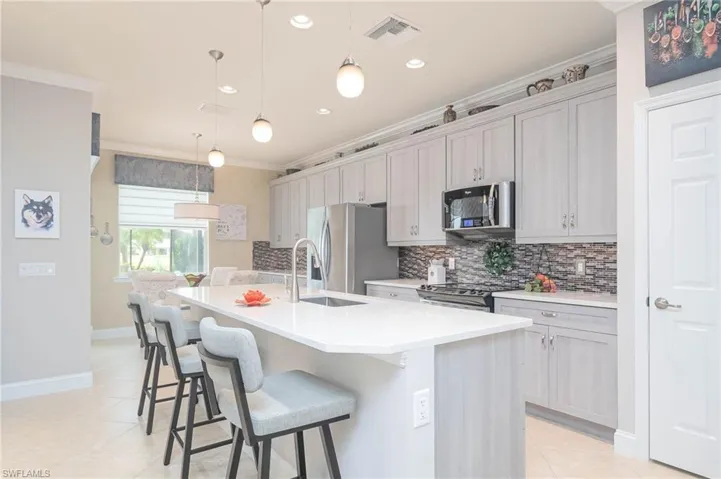 Kitchen featuring a center island with sink, decorative light fixtures, gray cabinets, and appliances with stainless steel finishes