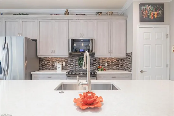 Kitchen featuring sink, decorative backsplash, crown molding, and stainless steel appliances.
