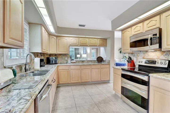 Kitchen with light tile patterned floors, appliances with stainless steel finishes, light brown cabinetry, and sink
