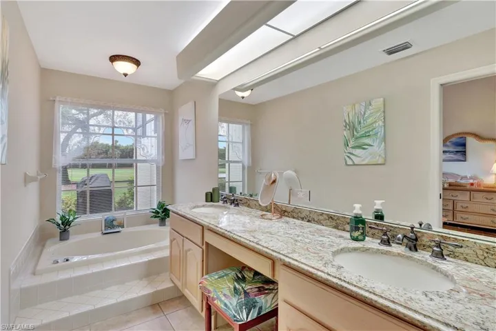 Bathroom with vanity, tile patterned flooring, a skylight, and tiled tub