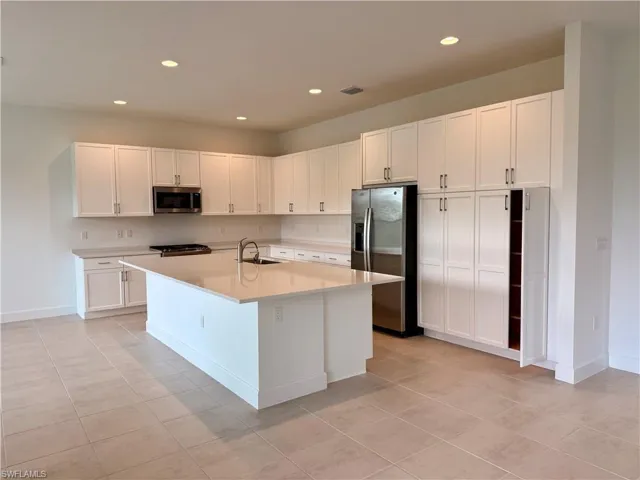 Spacious kitchen featuring an expansive central island, abundant white cabinetry, stainless steel appliances, and large format tile flooring