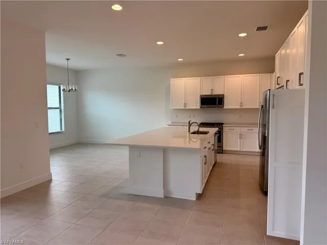 Modern kitchen featuring a large central island with an undermount sink, white cabinetry, stainless steel appliances, and recessed lighting