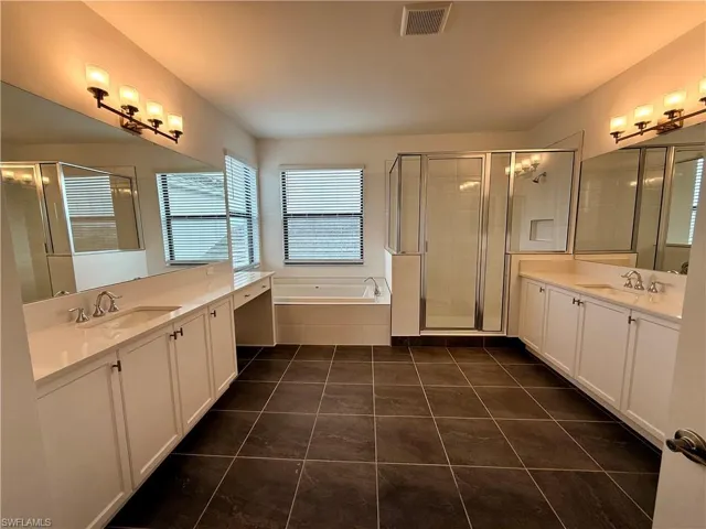 Spacious bathroom featuring twin vanities with integrated sinks, a built-in garden tub, a glass-enclosed shower, and dark tile flooring
