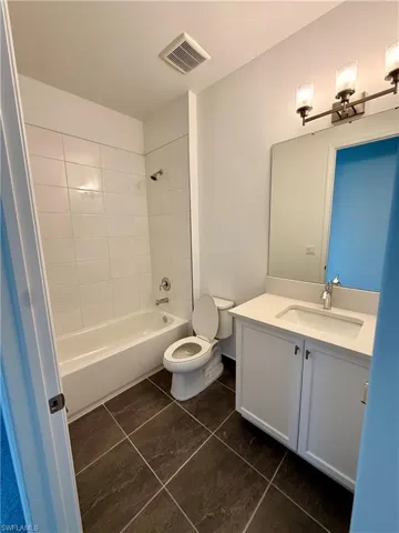 Full bathroom featuring a white tub/shower combination with subway tile surround, white vanity with integrated sink, rectangular mirror, and dark-toned tile flooring