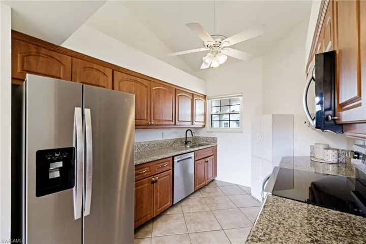 Kitchen with appliances with stainless steel finishes, brown cabinetry, light tile patterned flooring, a ceiling fan, and lofted ceiling