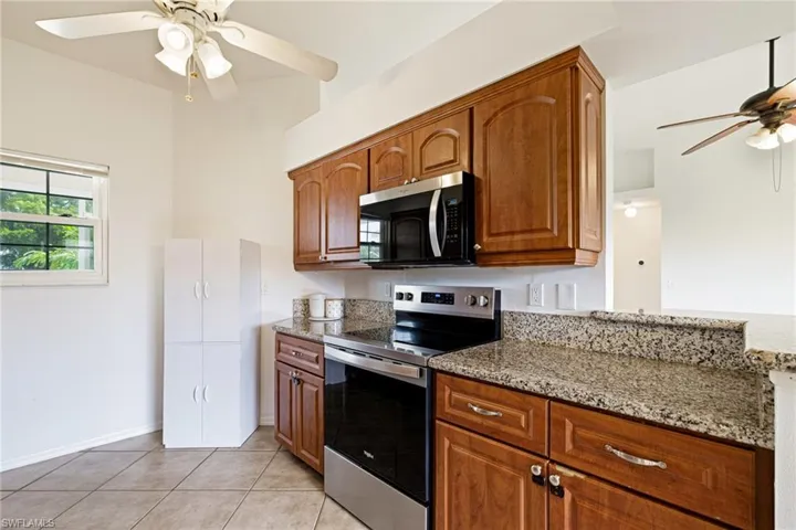 Kitchen featuring stainless steel appliances, a ceiling fan, light stone countertops, light tile patterned floors, and brown cabinetry