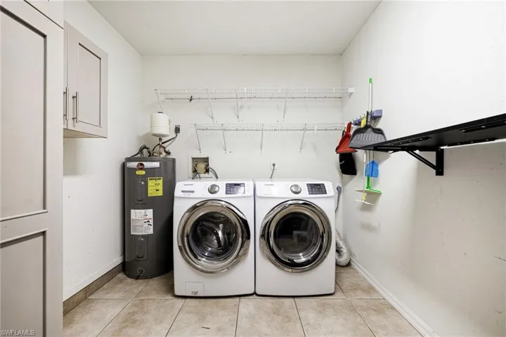 Laundry area featuring electric water heater, washer and clothes dryer, and light tile patterned flooring