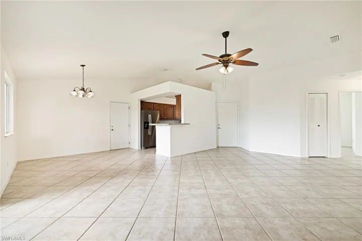 Unfurnished living room featuring lofted ceiling, a chandelier, ceiling fan, and light tile patterned flooring