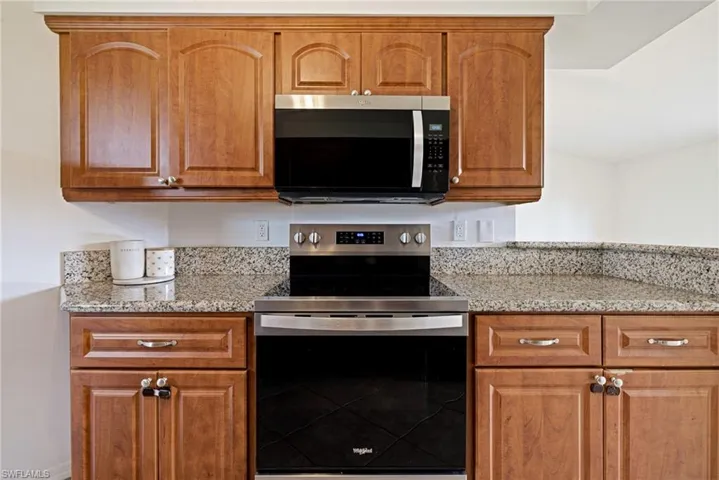 Kitchen featuring appliances with stainless steel finishes, light stone counters, and brown cabinetry